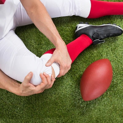 An American football player holding their knee on the field after an injury