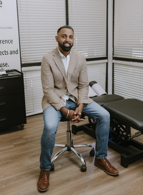 Dr. Gurj Kalay sitting on a stool in an adjustment room