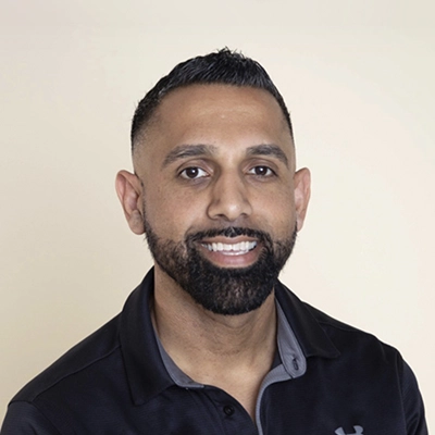A headshot photo of Dr. Gurj Kalay wearing a black clinic polo shirt against a light background.